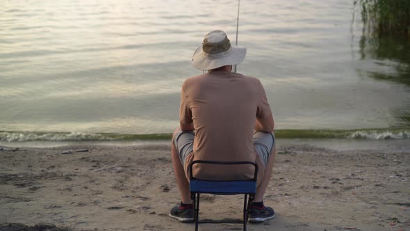 the View From the Back is a Man Fisherman at Dawn on the Lake Catching Fish with a Bait