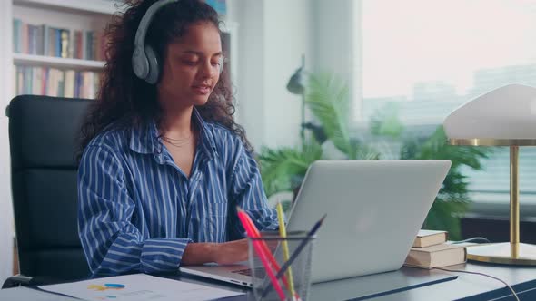 Young Indian Woman Freelancer in Wireless Headphones Typing on Laptop Keyboard