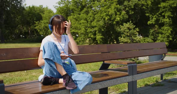 A Teenage Girl Listens to Music in Headphones Through an Online Smartphone Application