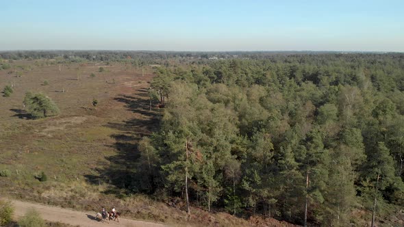 Aerial view of two horseback riders on a sand road entering the frame coming from a moorland landsca