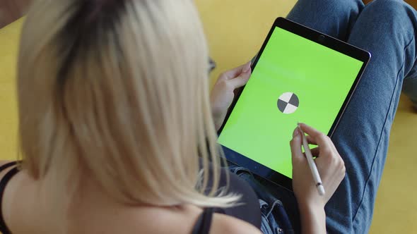 Female Artist is Sitting Sofa and Drawing with Stylus on Tablet with Chromakey Screen Back View