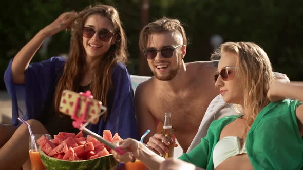 Bearded Caucasian Male with Tattoes Drinking Beer with Two Hot Females in Sunglasses with Cocktails