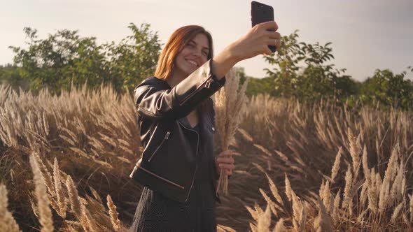 Attractive Fun Stylish Redhead Woman in the Field at Sunset Making a Selfie with a Bouquet of