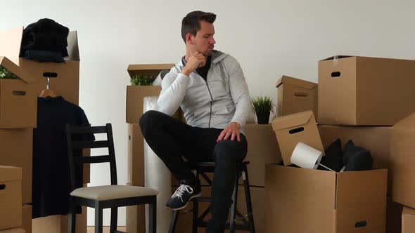 A Moving Man Sits on a Chair and Thinks About Something in an Empty Apartment, Surrounded By Boxes