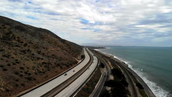 Aerial drone shot over the 101 freeway with cars next to the blue Pacific Ocean waves and California