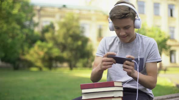 Teen Boy in Headphones Playing Mobile Game Instead of Homework, Procrastination