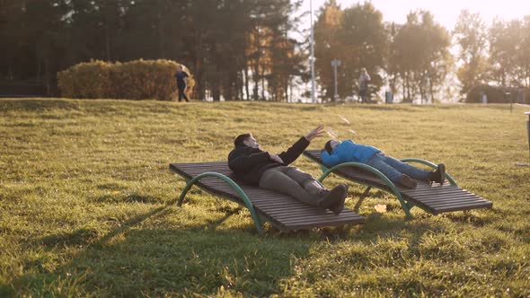 Family in Warm Casual Clothes Lie on Deck Chairs in Sunny Autumn Park