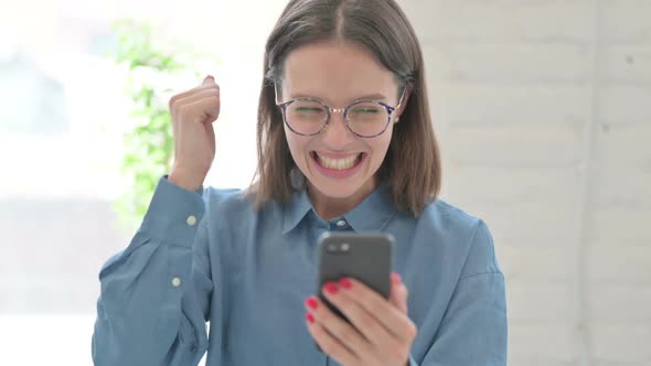 Young Woman Celebrating Success on Smartphone in Office