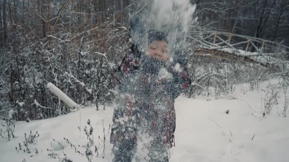 Teen boy throws snow in the winter forest