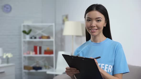 Female Volunteer Making Notes and Smiling on Camera