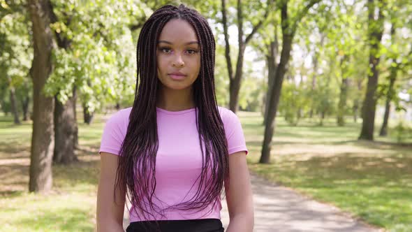 A Young Black Woman Looks at the Camera in a Park on a Sunny Day