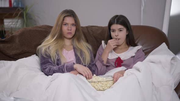 Front View Two Young Women Discussing Show Watching TV Throwing Popcorn to Camera