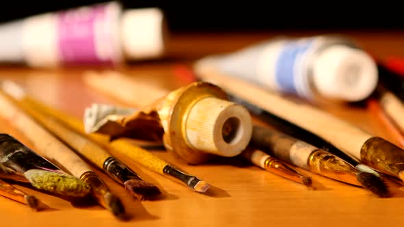 Paints and Brushes, Tubes of Paint on Wooden Table, Black Background, Cam Moves To the Right