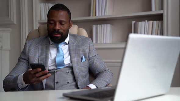 Black Businessman Is Surfing Internet By Cell Phone Sitting in His Working Office, Social Net