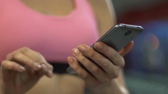 Active woman scrolling screen of smartphone in gym, using sports mobile app