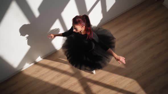 Ballerina in Black Tutu Gracefully Dances Against White Wall in Bright Sunlight
