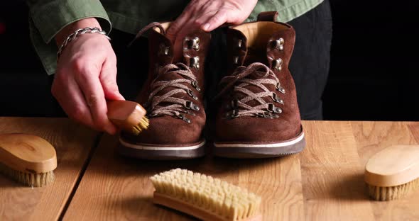 Man's hand clean suede shoes, boots with a brush on wooden background