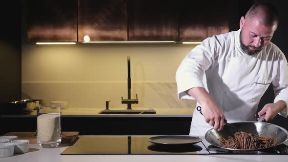 cook puts cooked noodles with vegetables on plate with tongs