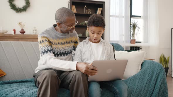 Positive African American Boy Explaining Grandfather How to Use Laptop and Internet Sitting Together