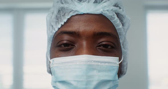 A Young AfricanAmerican Doctor with Medical Cap and Mask Looks Into Camera