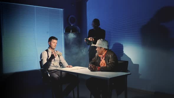 Interrogation Room in Smoke: Detective Showing Evidence of Drug Trafficking To Suspected Black Man