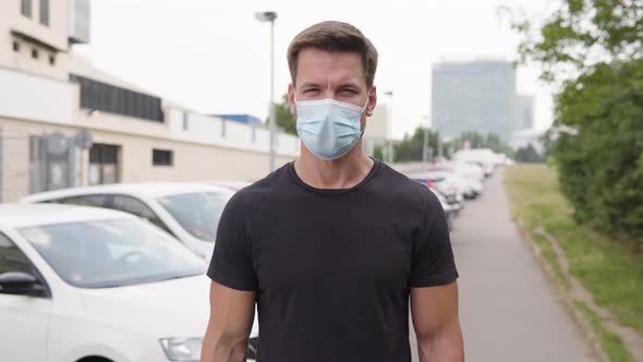 A Young Handsome Man in a Face Mask Talks To the Camera in a Parking Lot in an Urban Area