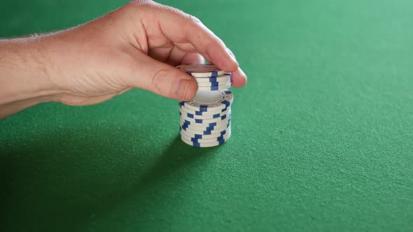 A man playing with red poker chips on a green table at a casino