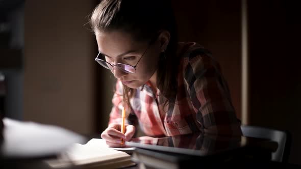 A young woman sits late at night for textbooks. Exam Preparation