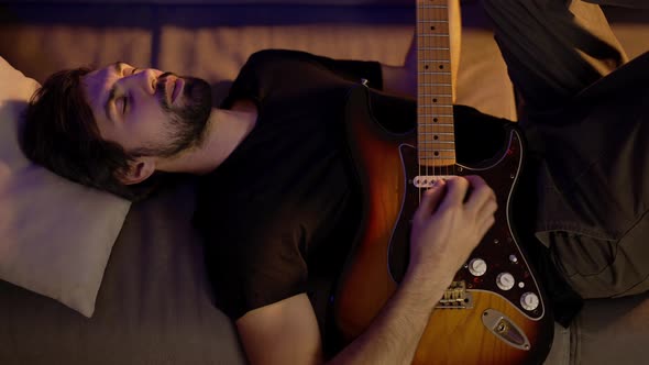 Man Playing on Guitar While Lying on Couch with Closed Eyes