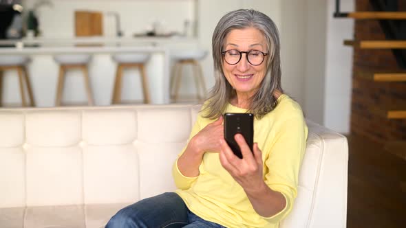 Positive Senior Mature Lady in a Yellow Jumper Talking Online on the Phone