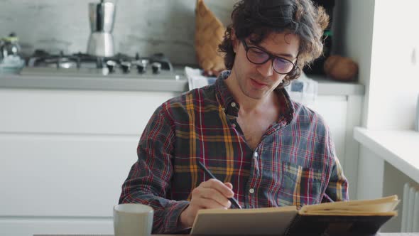 Concentrated adult man in a plaid shirt painting something in notepad