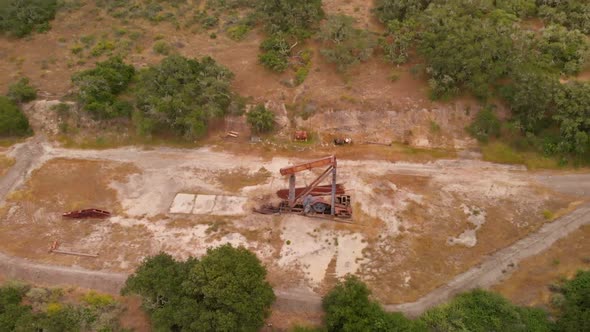 Abandoned Rusty Oil Pump Revealed Behind Rolling Hills with Drone