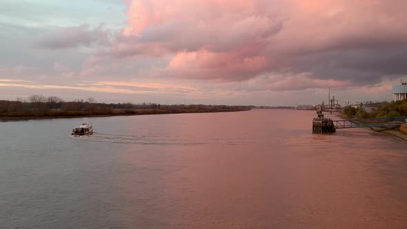 Drone captures a boat sailing away under pink light reflecting off the river and clouds.