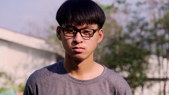 Portrait of a confident young man in glasses and casual gray t-shirt standing in a summer garden.