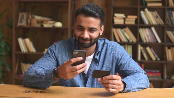 Confused and Disappointed Indian Man Using Smartphone and Banking Card for Shopping