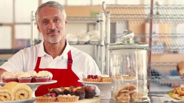 Happy server looking at camera with thumbs up behind cakes