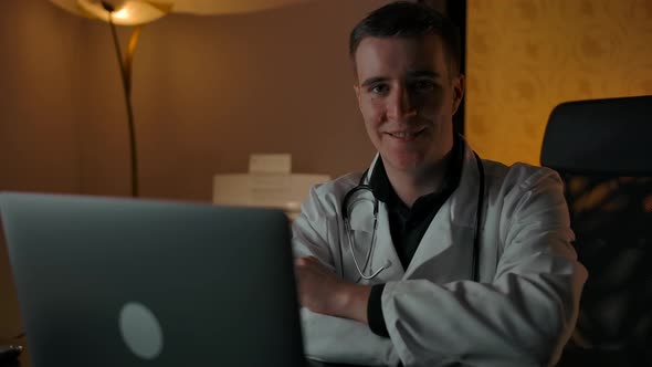 Smiling Doctor in Robe Behind Laptop Smiling at Camera