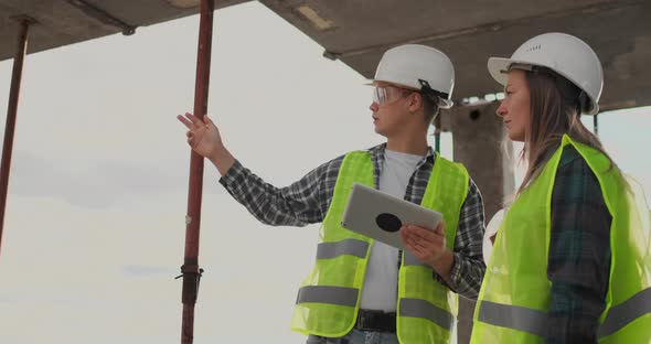 Construction Worker Man and Architect Woman in a Helmet Discuss the Plan of Construction of House