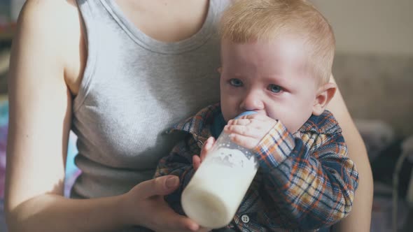 Mommy Feeds Adorable Little Baby From Bottle in Room Closeup