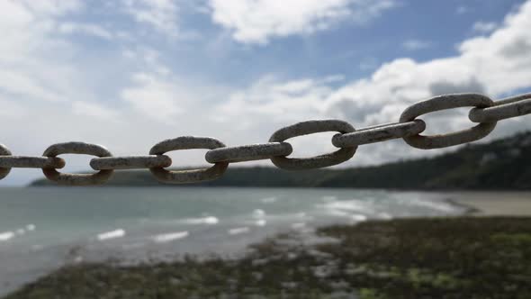 LOCKED OFF View Of Chain Link In Focus With Waves Hitting Laxey Beach In The Background