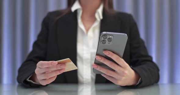 Young Woman Sitting at the Table and Pays for Purchases Online Using a Smartphone Enters Credit Card