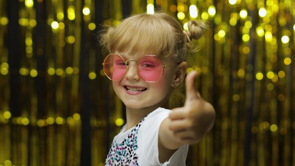 Child Show Thumbs Up, Smiling, Looking at Camera. Girl Posing on Background with Foil Golden Curtain