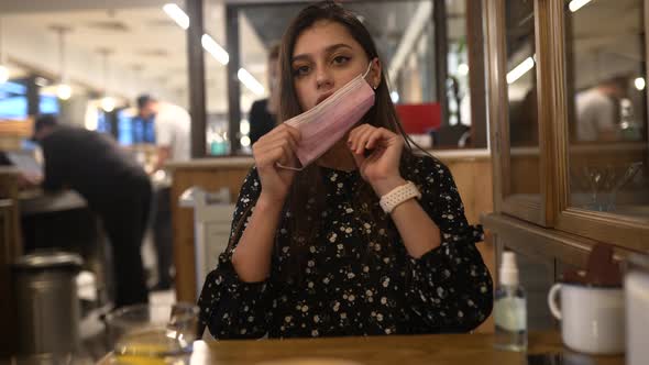 Attractive Young Woman Putting on Protective Mask in the Cafe