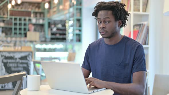 African Man with Laptop Looking at Camera in Cafe