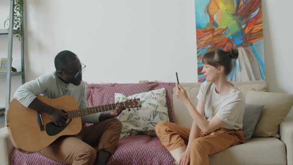 Afro Man Playing Guitar and Singing as Wife Filming Video with Phone