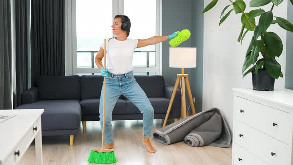 Woman in Headphones Cleaning the House and Having Fun Dancing with a Broom and Washcloth