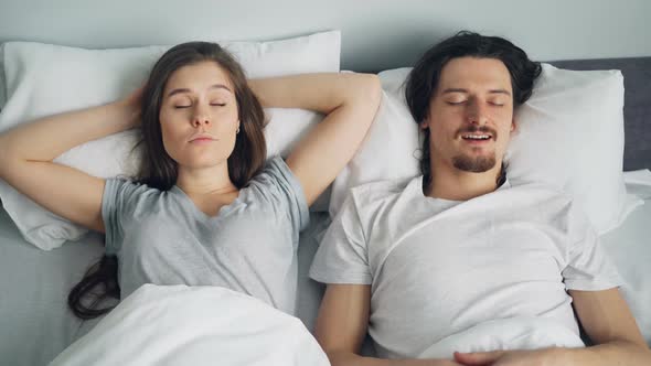 Angry Wife Covering Face with Pillow While Sleeping Husband Snoring in Bed