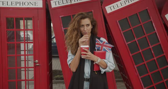 Attractive Girl Walking on a Background of Red British Phones. Drinks Coffee and Sightseeing