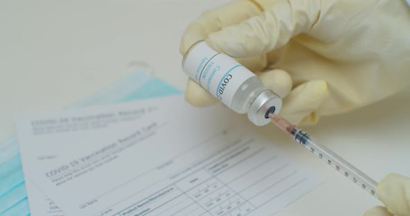 Close Up of Hand Filling a Syringe with Liquid From a Vial with a Label Reading Covid19 Vaccine