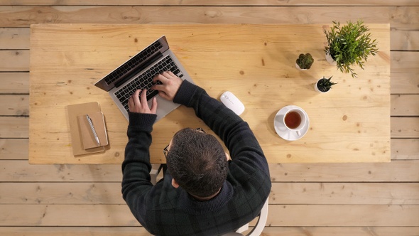 Young bearded man drinking coffee or tea while working on laptop